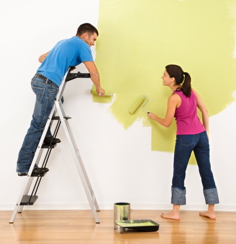 Attractive young adult couple painting interior wall of house.